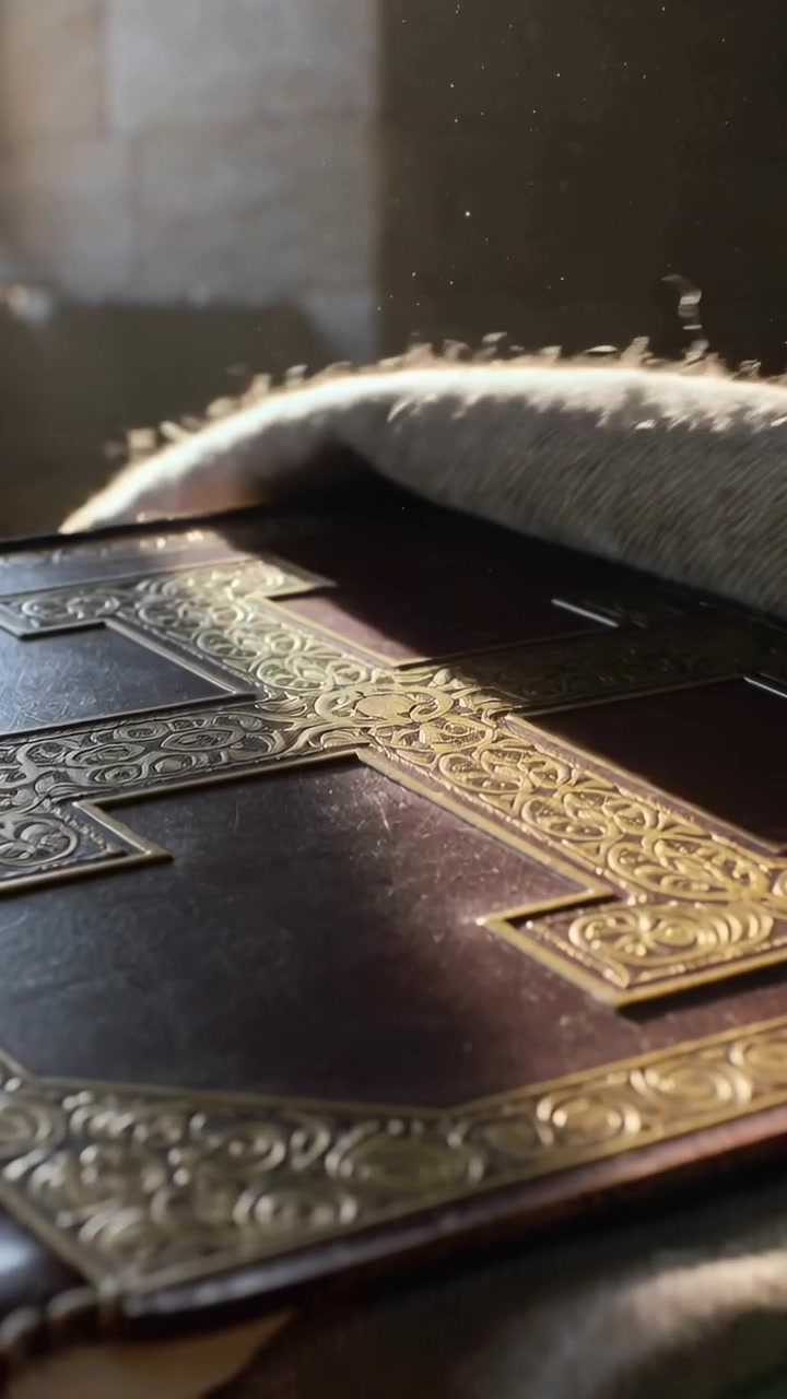 Vertical video: Sunlight nudging folded cloth sliding aside on wood table, showing book metal cross