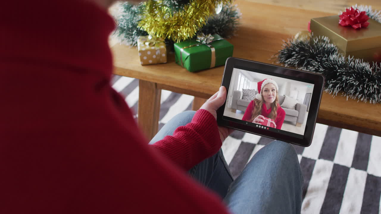 Uomo albino che saluta e usa un tablet per una videochiamata di Natale con una donna sorridente sullo schermo
