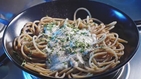 cooked spaghetti pasta in a plate with greek yogurt sauce, topped with chopped parsley and black pepper