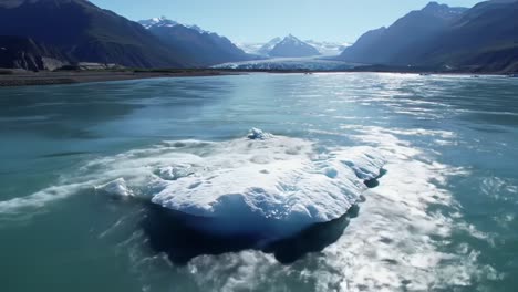 a serene glimpse of a majestic iceberg float in crystal-clear waters surrounded by breathtaking mountain scenery under a bright blue sky