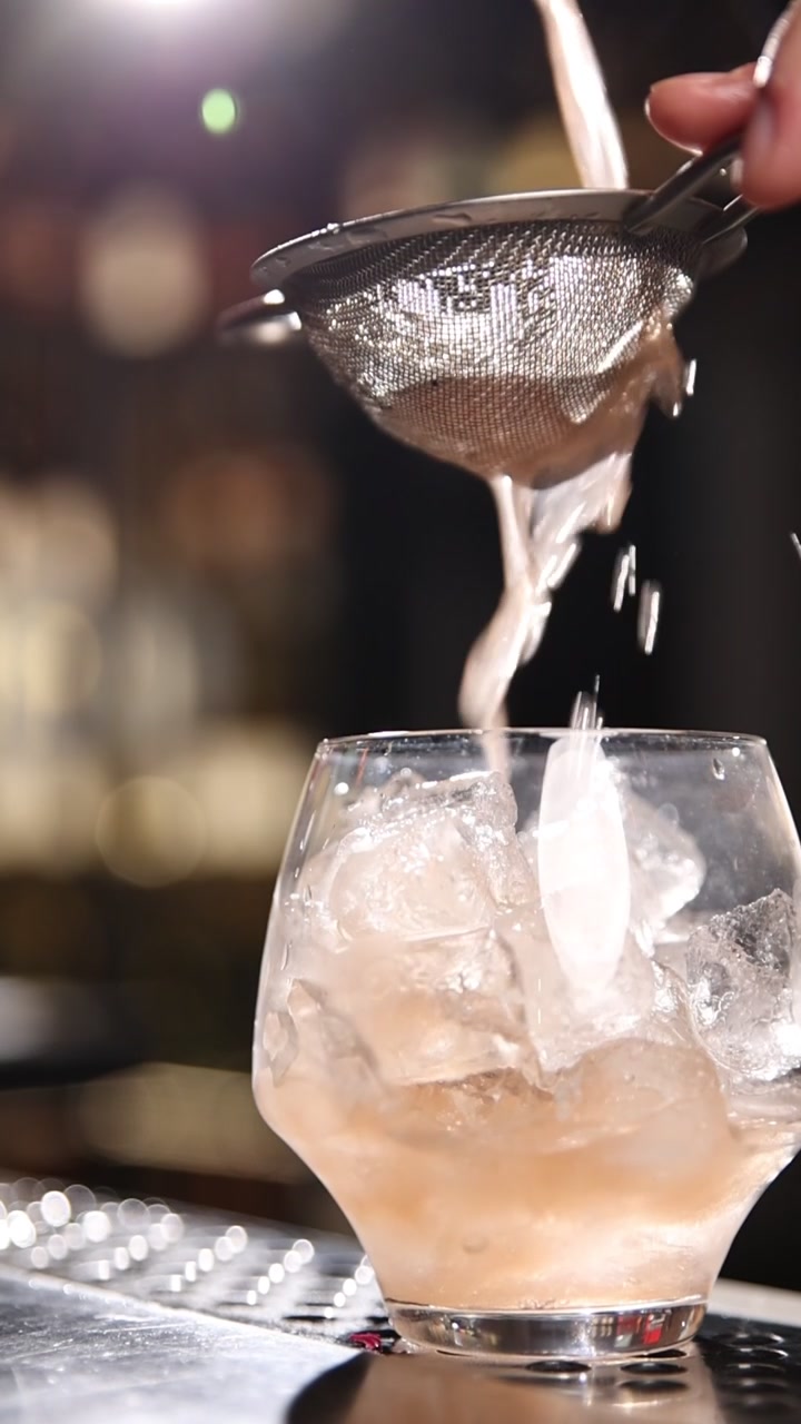 Cocktail rinfrescante versato e filtrato in un bicchiere con ghiaccio