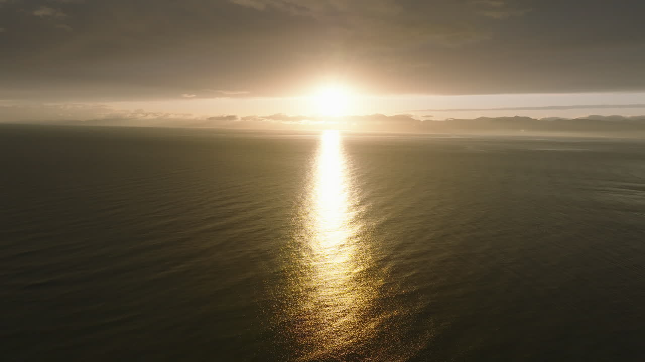 Aerial drone shot flying over the the Tasman Bay ocean towards the coastline during the very early hours of morning as the sun starts to rise