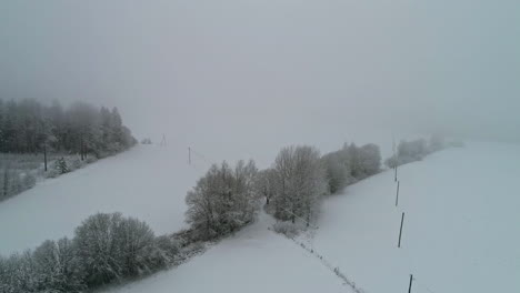 backwards drone dolley shot during a snow shower and fog over a winters landscape