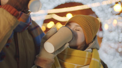 pareja romántica tomando café y besándose en la calle con luces navideñas