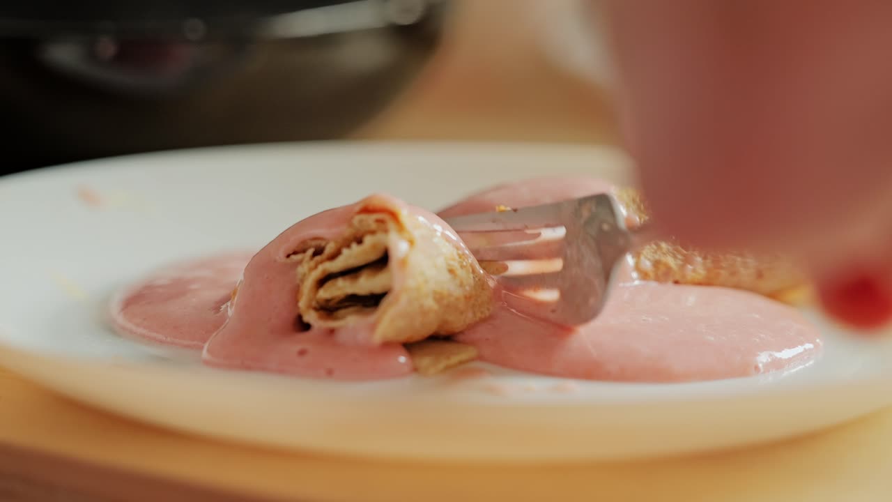Close up of pancake sliced with fork, dripping pink strawberry banana sauce