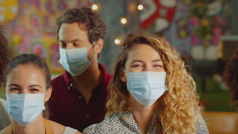 portrait of multi-cultural group of friends wearing face masks enjoying night out in bar or club