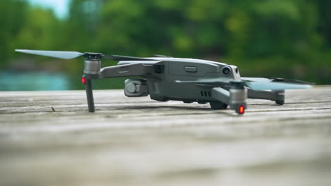 drone perched on a wooden dock boots up, the propellors begin spinning, and it takes off