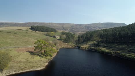 aerial shot panning left over kinder reservoir water close to trees revealing a national trust estate in the distance in the kinder scout valley