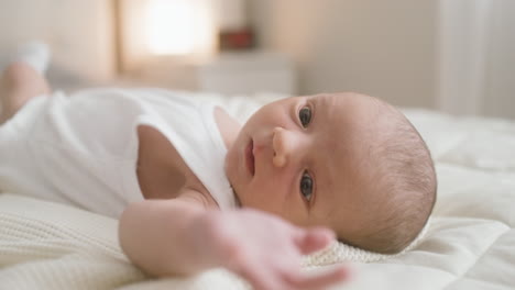 close up view of a baby in white bodysuit lying on bed moving his arms 1