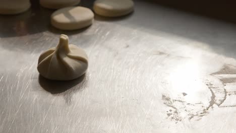 Cook-puts-raw-dumplings-on-counter-top,-closeup-handheld-view