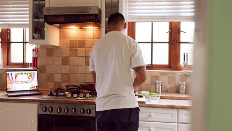 Man-cooking-food-from-recipe-on-laptop