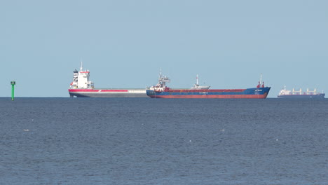 un buque de carga rojo y blanco navega en un mar azul tranquilo bajo un cielo despejado, posiblemente un petrolero, con una boya de navegación visible, que simboliza el transporte marítimo y el comercio global