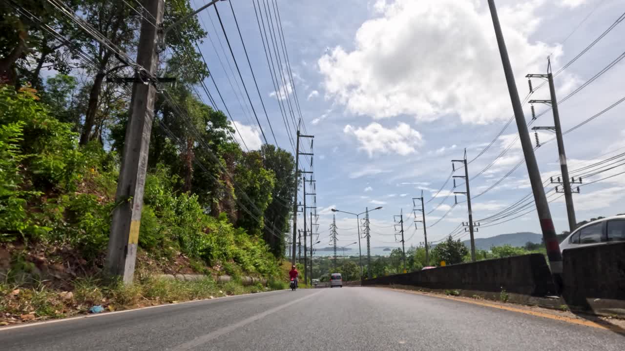 Motorcyclist travels on tropical urban street, lush greenery, bright daylight, low-angle, smooth camera movement