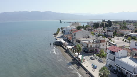 Low-flight-of-city-ocean-waterfront-on-Greek-Aegean-Sea,-distant-pier