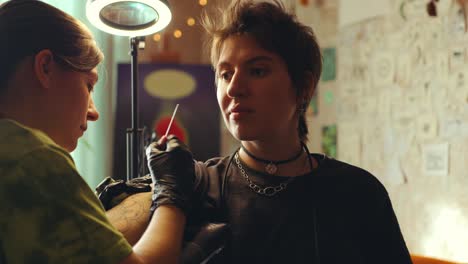 young woman getting handpoke tattoo on arm from female tattoo artist