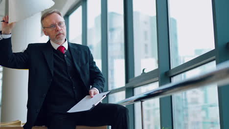 angry businessman in the office. mature man in elegant suit becomes nervous while working in his company. senior entrepreneur with folder by the window.