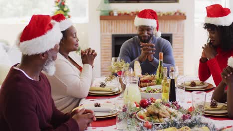 african american family wearing santa hats holding hands and praying