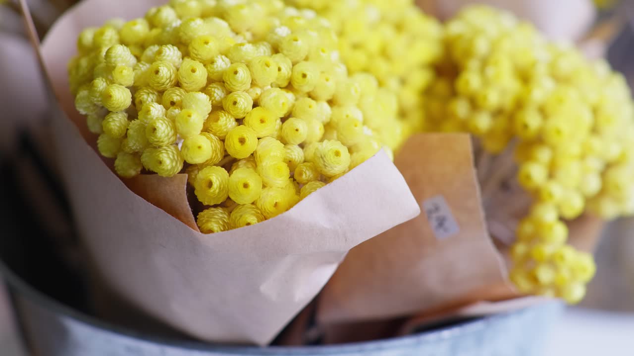 Smooth right-to-left dolly shot with a rack focus from background to foreground, showcasing charming bouquets of yellow dried flowers in a rustic flower shop