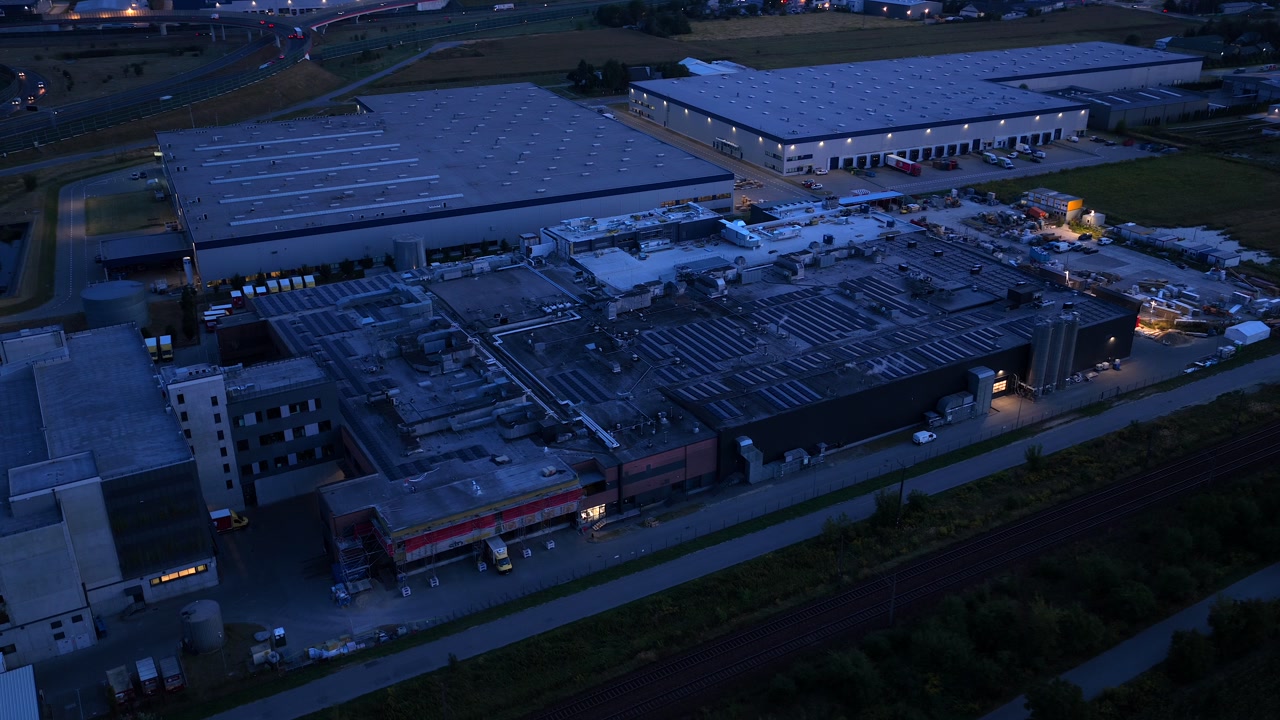 Aerial drone view of modern warehouses and industrial buildings in Warsaw, Poland, captured at dusk with surrounding infrastructure and logistics facilities.