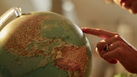 a person's hand pointing at a world globe
