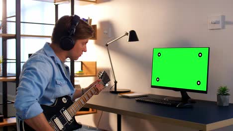 hombre con auriculares y computadora tocando la guitarra