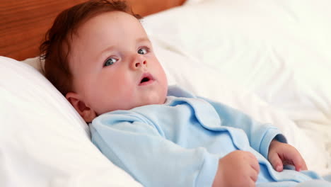 baby boy in blue babygro lying on bed