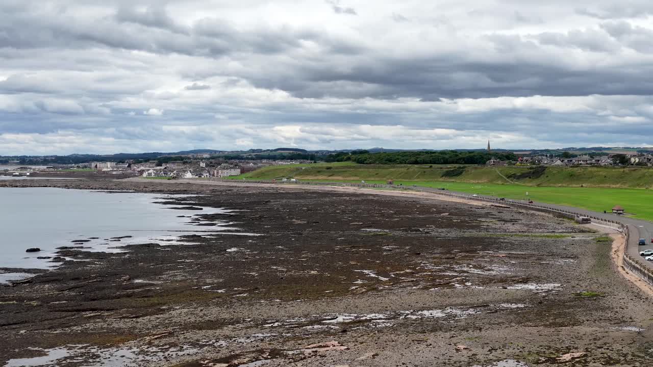 Aerial camera pans across Dundee coastline, green fields, and cloudy sky, revealing coastal townscape