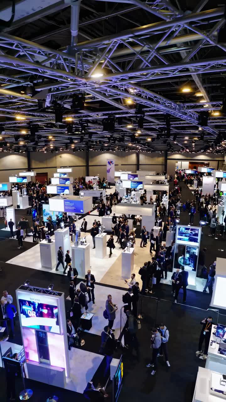 High-angle view of a bustling tech expo with numerous booths and attendees, capturing the dynamic