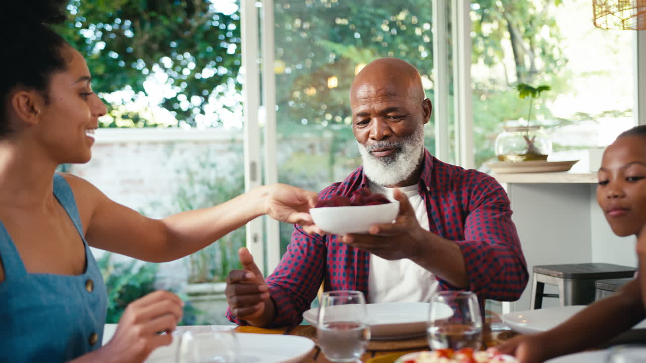 Close Up Of Multi-Generation Family Sitting Around Table Serving Food For Meal At Home Together
