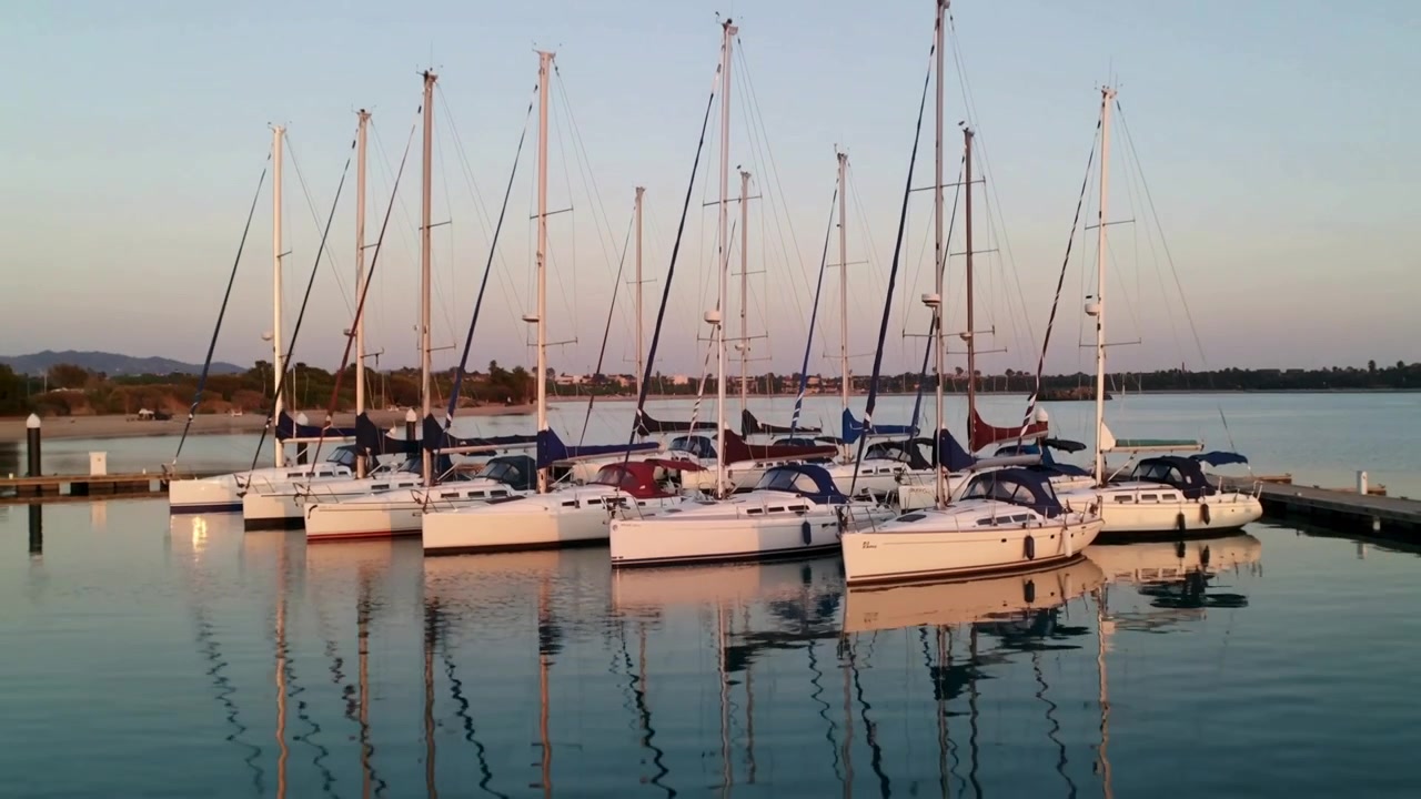 En reculant la caméra, une rangée de voiliers amarrés ballotant dans la marina, révélant le quai et les reflets.