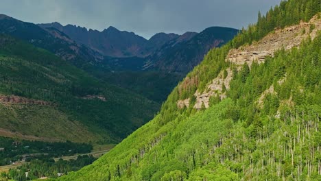 aerial tracking pan left of ridges and forested slopes near vail with dark moody sky and summer greens