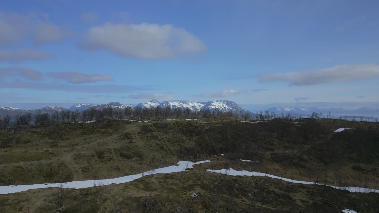 Farmland nestled in rolling hills with snow-capped mountains and clear skies in the background