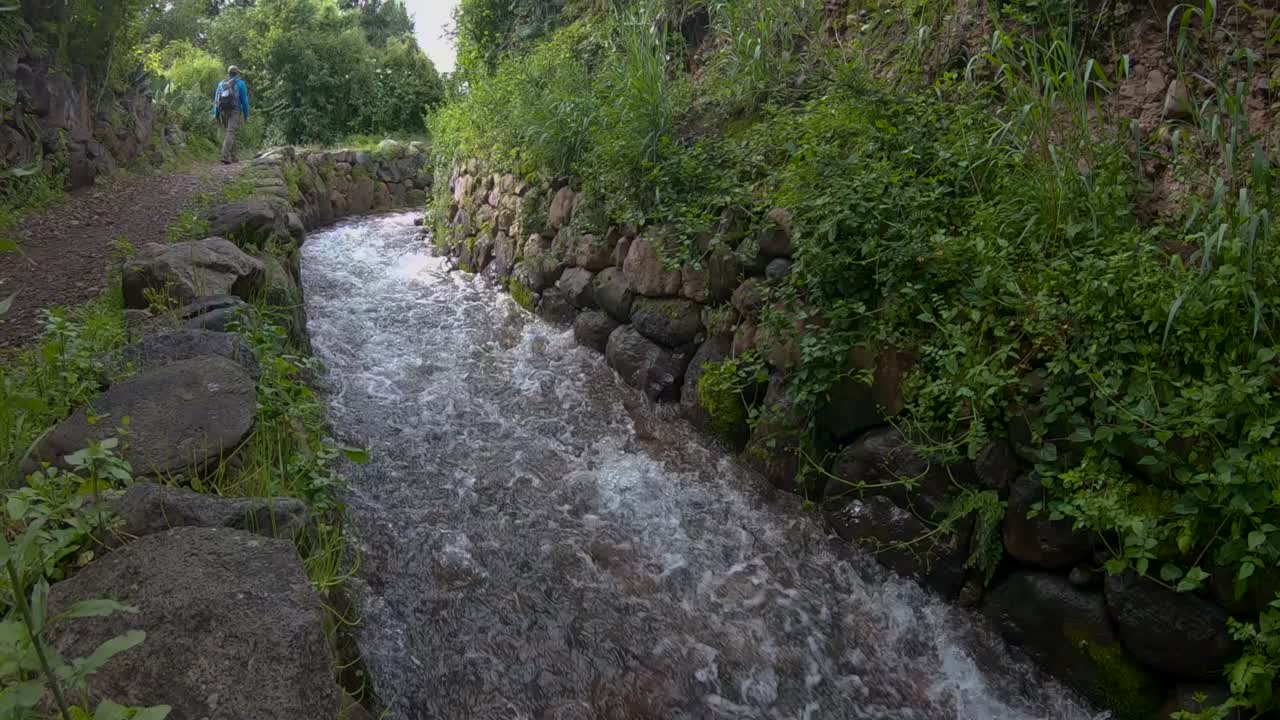 turistas caminando por un sendero rodeado de mucha vegetación junto a un arroyo de agua clara en el valle sagrado de los incas, ubicado en cusco, perú