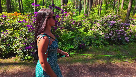 slow motion side shot of a hot girl wearing sunglass and walking in a beautiful park with flowers on the background