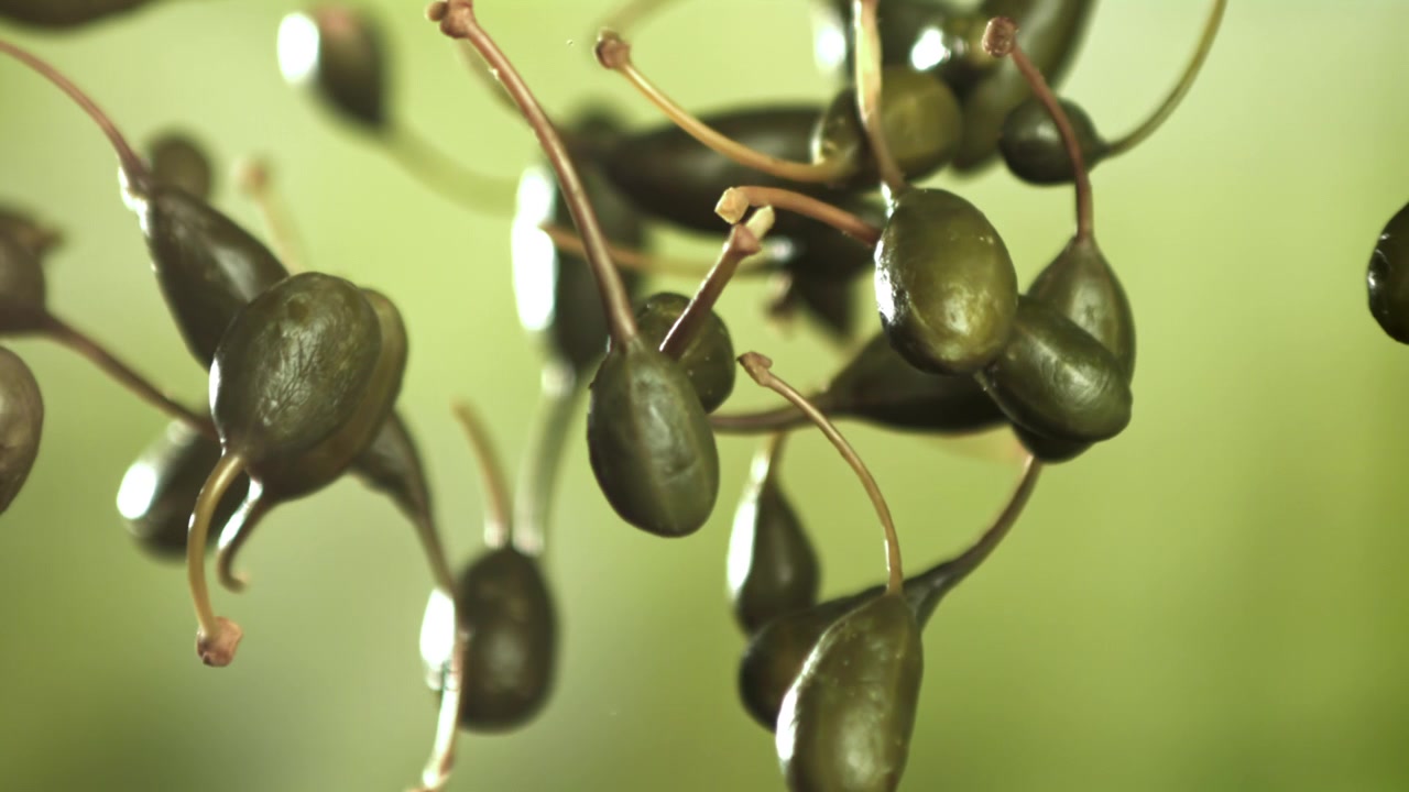 Bacche di cappero fresche che cadono al rallentatore su sfondo verde