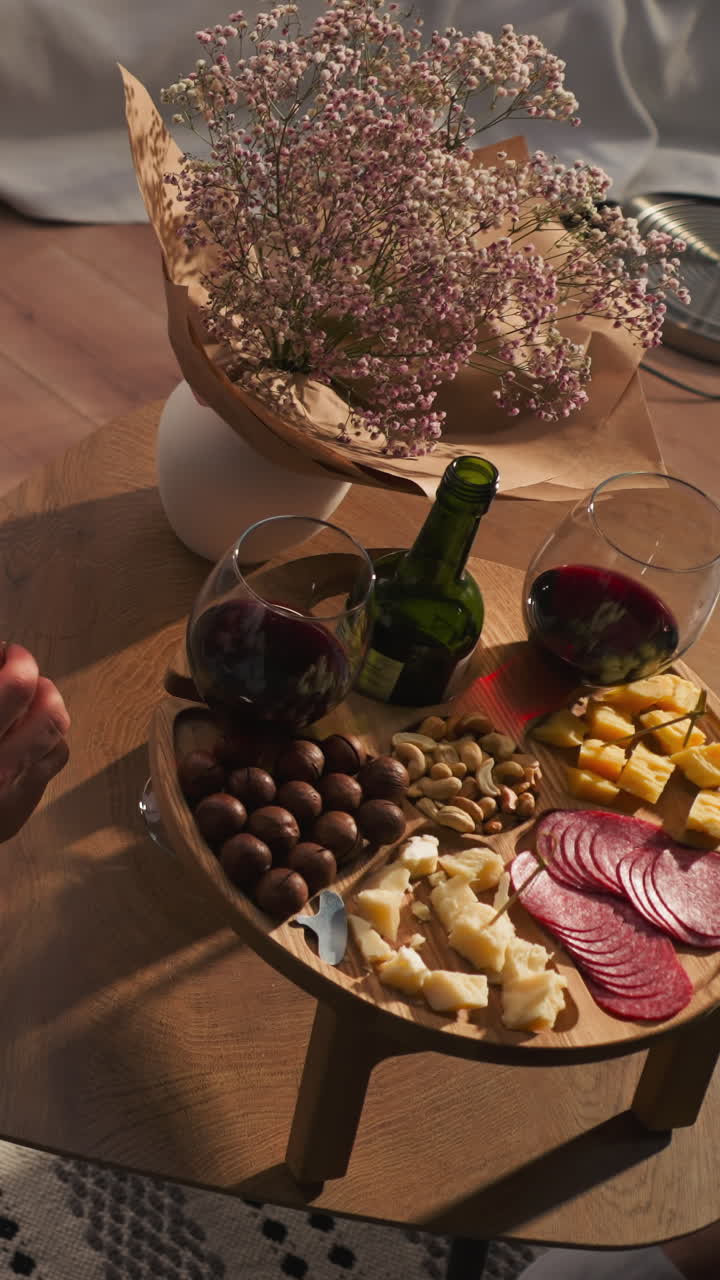 Man enjoys snacks at wooden wine table. Relaxed guy in soft robe eats gourmet snack complemented by glass of wine. Relaxation evening in glamping house