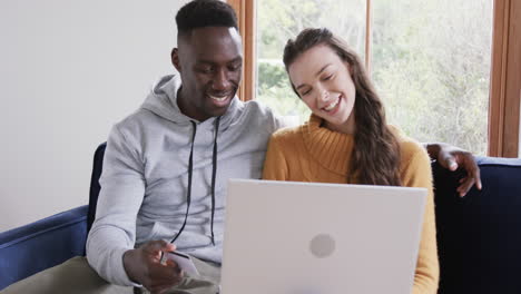 Happy-diverse-couple-sitting-on-sofa-and-having-video-call-in-sunny-living-room,copy-space