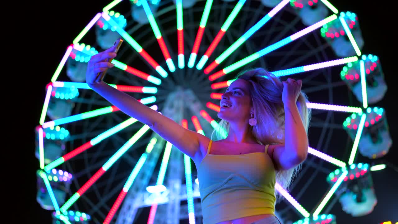 Woman taking selfie in front of Ferris wheel at night