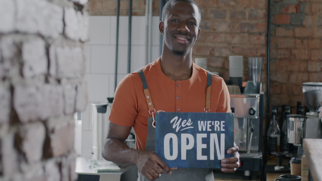 Smilende barista holder åbent-skilt