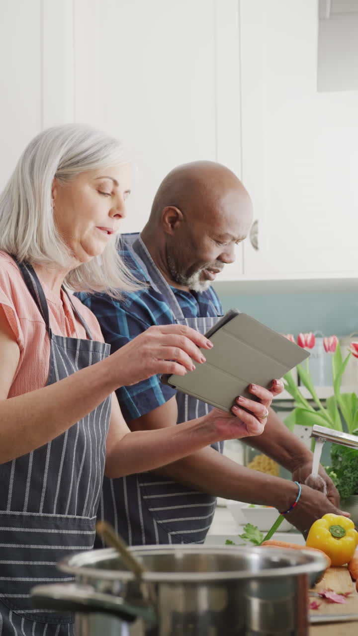 video vertical de una pareja de ancianos feliz y diversa preparando comida juntos usando una tableta en la cocina