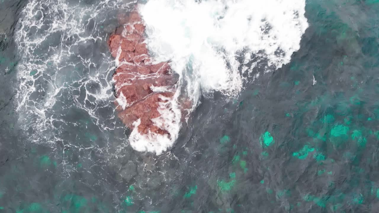 las olas chocan contra las ásperas rocas rojas en medio de aguas turquesas y negras