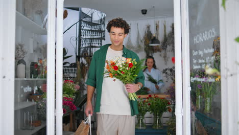 el comprador de flores relajado deja la tienda de plantas en la ciudad de verano. el hombre africano disfruta del ramo