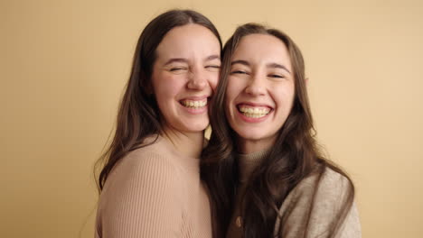 cheerful women hugging each other near beige wall