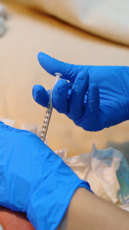 medic wearing blue latex gloves give a shot to a newborn child. injection right after birth. close up. vertical video