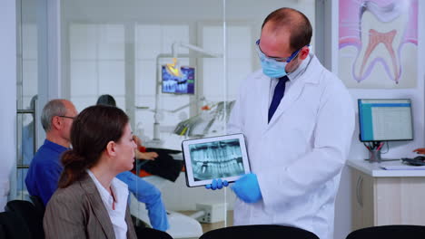 stomatologist pointing on digital screen explaining x-ray to woman