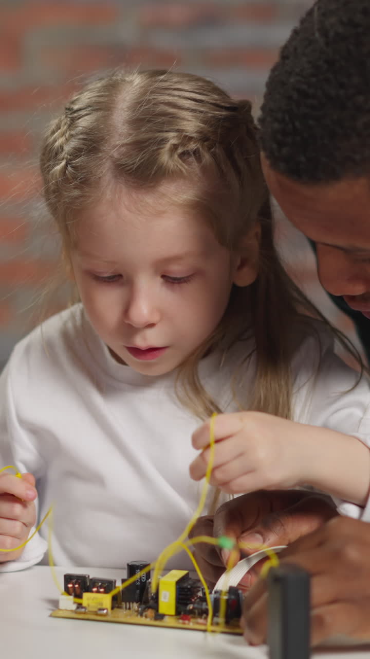 Schoolgirl and black man engineer work with chip studying electricity effect and green lamp lights while Asian guy fixes hard disk drive at table closeup