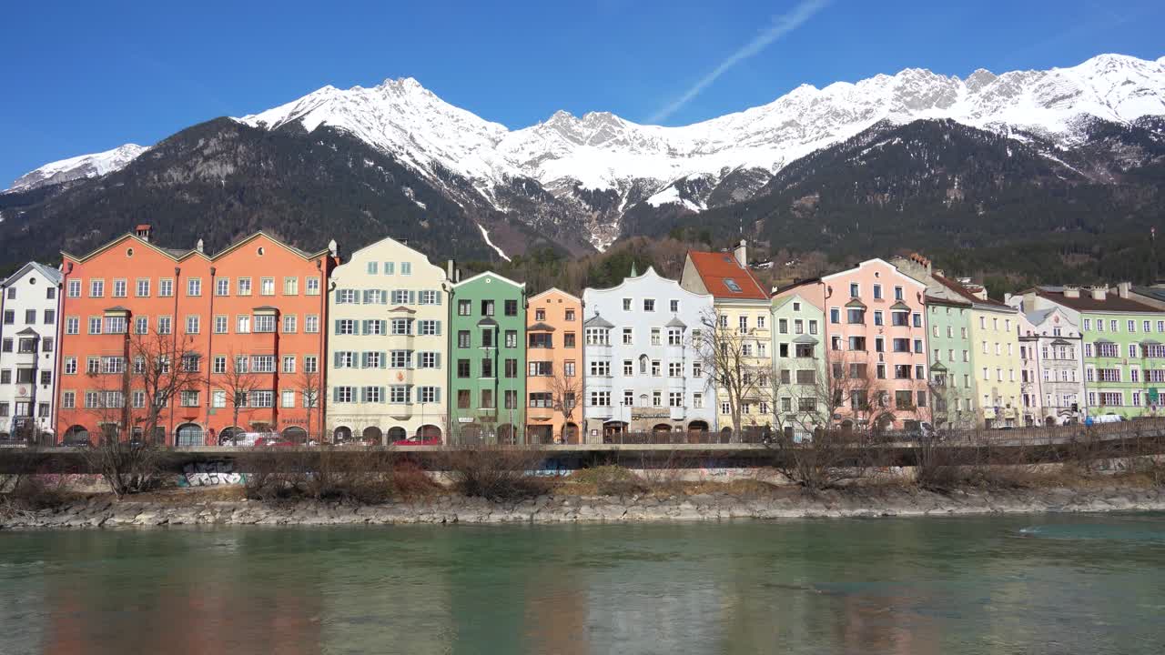 Färgglada traditionella byggnader vid floden Inns strand med snöklädda alptoppar i Innsbruck, Österrike.