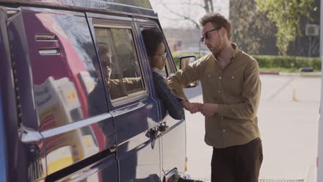 an young woman and a young man have a conversation while refueling their van