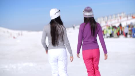 Dos-Mujeres-Jóvenes-Caminando-En-Una-Estación-De-Esquí-De-Invierno