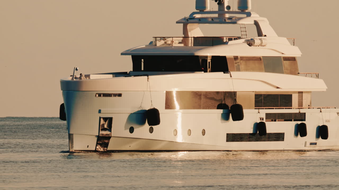 Vista laterale di un moderno yacht di lusso che solca le acque calme del mare con un faro in lontananza